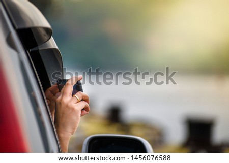 Hand of girl take a photo by smartphone while sitting in the car. Woman smiling while sitting on the passenger seats in the car. Girl is using a smartphone She makes a photo of nature.