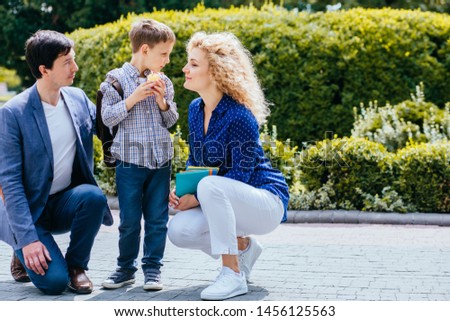 Mature parents saying goodbye to their little child near school. Happy family dad and mom holding books, cute preteen son biting apple. Trust, family value concept. Copy space.
