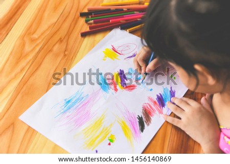 Girl painting on paper sheet with colour pencils on the wooden table at home / child kid doing drawing picture and colorful crayon