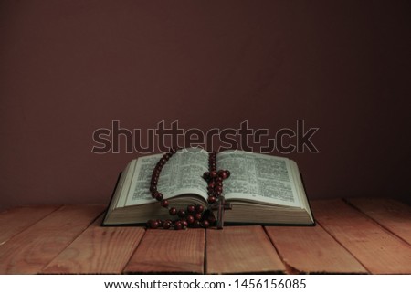 Open Holy Bible and beads on a old wooden table. Beautiful red wall backgroround. Religion concept.