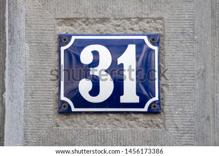 Vintage style house number 31. Blue metal sign on stone wall.