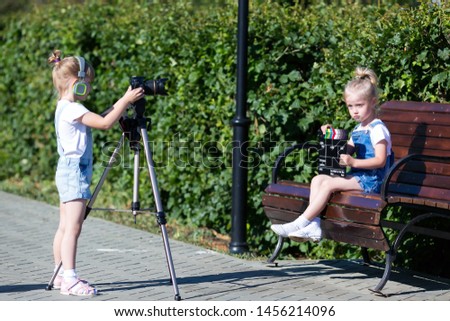 Two girls on the street make a video the Internet, record a video blog for the camera. Children with photo appart in a city park