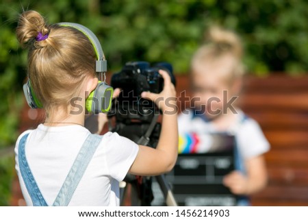 Two girls on the street make a video for the Internet, record a video blog for camera. Children with photo appart in a city park