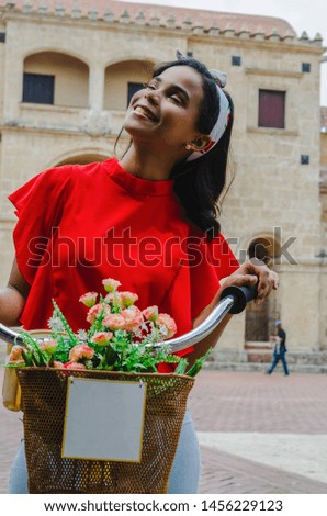 Outdoor portrait of young beautiful girl 19 to 25 years old posing in street. Brunette. riding a retro styled bicycle. Wearing red blouse With a penetrating camera look. City lifestyle. Fashion