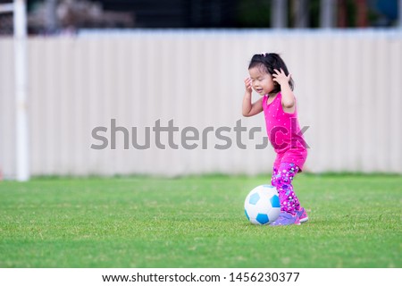 Asian baby child girl playing blue-white foodball in the playground. In the evening. She wearing a pink dress and purple shoe. She used both hands to shriek the hair. Baby ages 2 years 5 months.