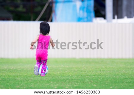 Asian baby child girl playing blue-white football on the playground in the evening. She is running, kicking the ball. She wearing a pink dress and purple shoe. Baby ages 2 years 5 months.
