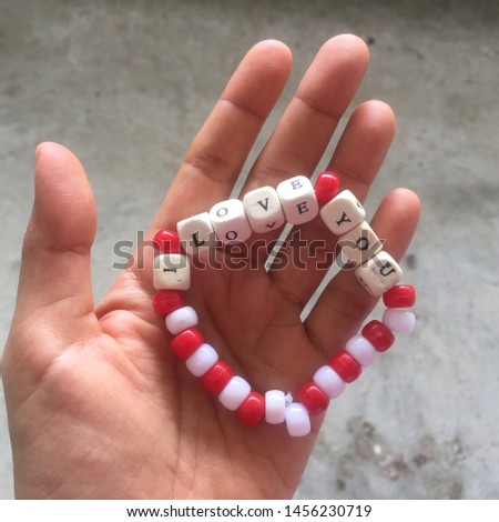 woman hand holding a bracelet bead red and white color with I love you word 