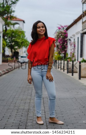 Outdoor portrait of young beautiful girl 19 to 25 years old. Brunette. posing in the middle of a colonial street with cobblestones. Wearing red blouse City lifestyle. Female fashion concept.