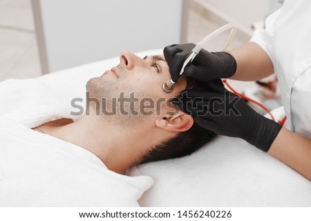 The cosmetologist makes the procedure Microdermabrasion of the facial skin of a man in a beauty salon.Cosmetology and professional skin care. Royalty-Free Stock Photo #1456240226
