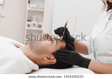 The cosmetologist makes the procedure Microdermabrasion of the facial skin of a man in a beauty salon.Cosmetology and professional skin care. Royalty-Free Stock Photo #1456240235