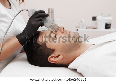 Skin care of ultrasound facial peeling. Ultrasonic cleansing procedure. Crop of beauty treatment of man. Beauty skin care cosmetology in spa salon.  Royalty-Free Stock Photo #1456240331