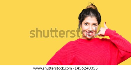 Young beautiful woman wearing red sweater and bun smiling doing phone gesture with hand and fingers like talking on the telephone. Communicating concepts.