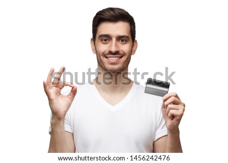 Portrait of young smiling man, holding credit card and showing okay sign, isolated on white background