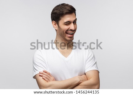 Young cheerful man winking while flirting, isolated on gray background