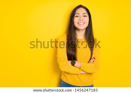 Beautiful brunette woman over yellow isolated background happy face smiling with crossed arms looking at the camera. Positive person.
