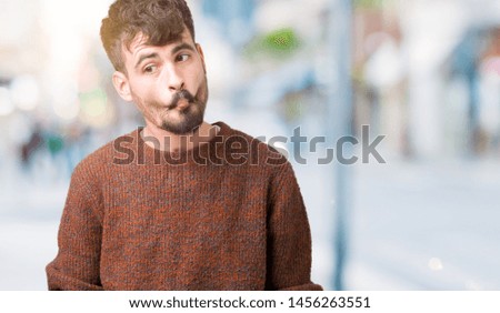 Young handsome man wearing winter sweater over isolated background making fish face with lips, crazy and comical gesture. Funny expression.