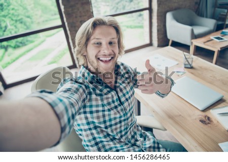 Close up photo of cheerful guy with blonde hair laughing wearing checkered plaid shirt in industrial