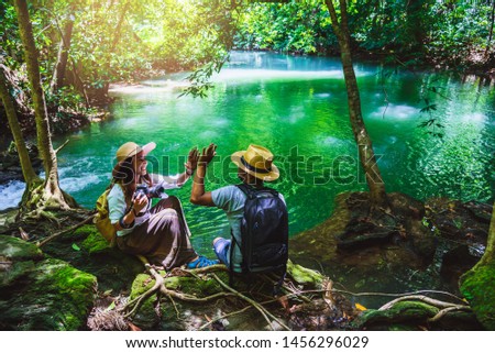 couples with backpacks sitting and relax on the rocks. travel nature in greens jungle and enjoying view in waterfall. Tourism hiking nature study. taking pictures of nature on holiday. emerald streams