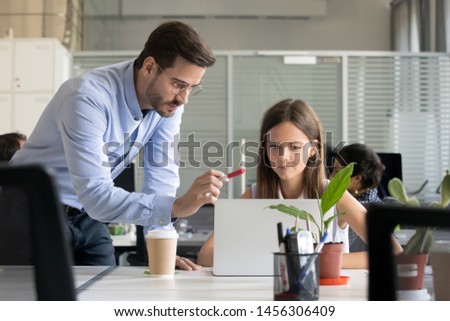 Serious male manager in glasses teach young female intern working at laptop, explain issues pointing, man trainer or coach instruct girl trainee helping with project, give instructions or correcting Royalty-Free Stock Photo #1456306409