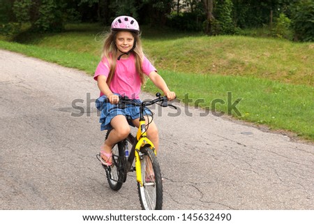  little girl in helmet learning to ride a bicycle on empty street