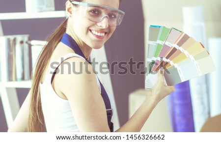 Young woman holding a color swatch with a painter painting .