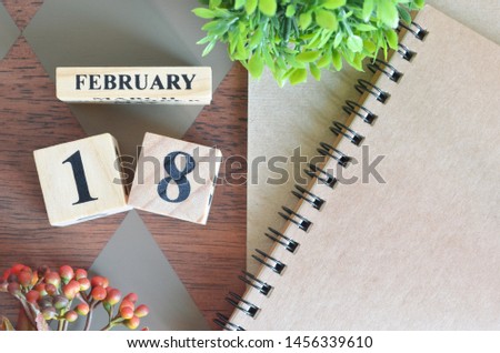 February 18. Date of February month. Number Cube with a flower and notebook on Diamond wood table for the background.