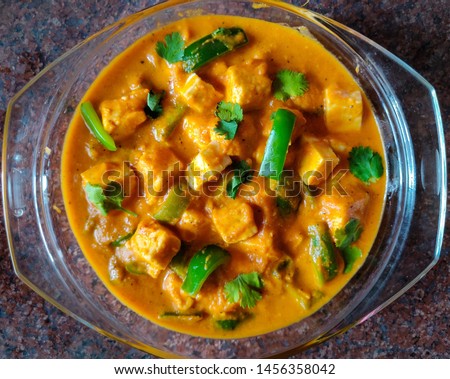  Close up, flat lay picture of indian cottage cheese dish with tomato and onion gravy, with capsicum and coriander garnish served in a glass dish also known as 'Shahi Paneer'.