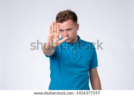 Angry man in blue shirt showing hand. Stop this, stay away from me. Studio shot