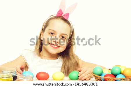 small baby girl or cute child with happy face and rabbit pink ears on blonde head with colorful easter eggs on table isolated on white background.