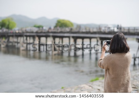 Young Asian woman short hair tourist is taking a picture by camera at Togetsu-kyo Bridge in Arashiyama district, Kyoto, Japan. Travel in Japan concept.