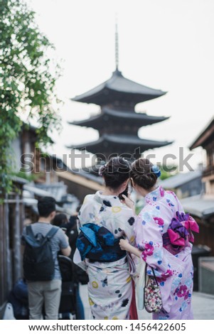 Young Asian couple woman wearing Japanese traditional kimono are taking a photo by smart phone at the urban old  town street with more traveler in Kyoto, Japan. Yasaka Pagoda landmark.