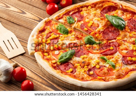 Delicious hot homemade pizza on the wooden table. Pizza - Fresh homemade pizza with pepperoni, cheese and tomato sauce, tomatoes, sweet corn and basil with copy space.