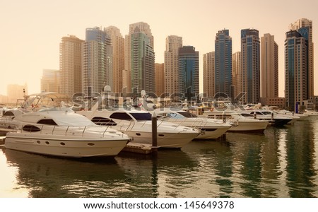 Luxurious Yachts and Boats in Front of Dubai Marina Skyscrapers, at sunset. All the logos and trade names are removed from the picture.