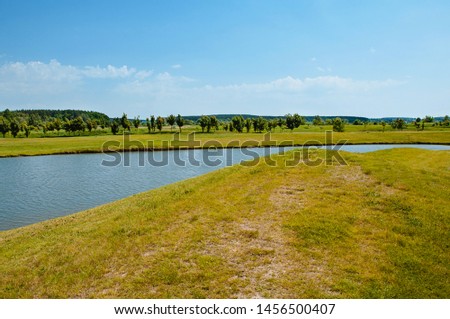 Lake on the golf course. Beautiful pheasant, blue cloudy sky, trees and bushes on the golf course.