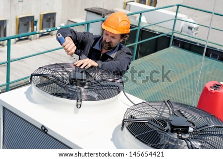Air Conditioning Repair, repairman on the roof fixing huge air conditioning system. Model is actual electrician.  Royalty-Free Stock Photo #145654421