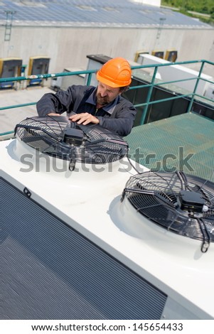 Air Conditioning Repair, repairman on the roof fixing huge air conditioning system. Model is actual electrician.  Royalty-Free Stock Photo #145654433