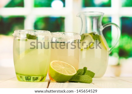 Citrus lemonade in pitcher and glasses on wooden table on window background