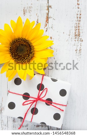 Greeting card with a bouquet of flowers with a sunflower with a wrapped box with a gift on a light wooden background with space for congratulations text. Happy birthday to you!