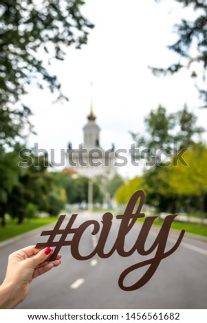 Letters city in woman hand on a city background. Hashtag city.