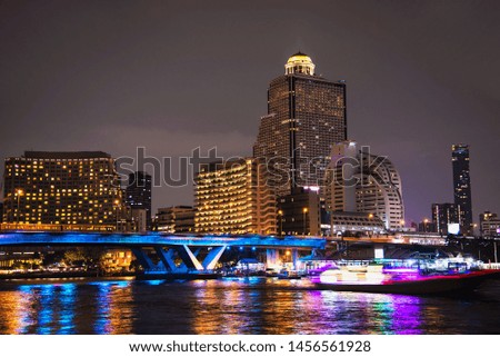 Colorful night picture of Asian city - blue light bridge over big river and building background in Bangkok Thailand