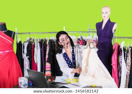 Picture of young female fashion designer holding a fabric while sitting in the studio over green screen background