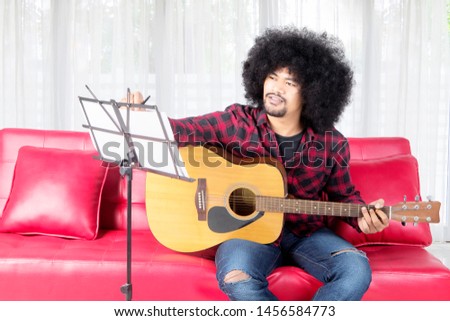 Picture of young musician writing a song while playing a guitar at home