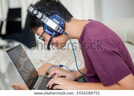 Picture of Asian preteen boy using a laptop for playing online games and wearing headphone at home