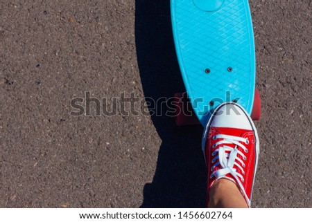 Close up of feet of a girl in red sneakers and blue penny skate board with pink wheels on the background. Urban scene, city life. Sport, fitness lifestyle.
