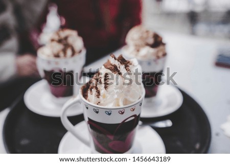 Cups of hot chocolate milk, whipped cream, marshmallows and cacao powder on a black and white serving tray. 