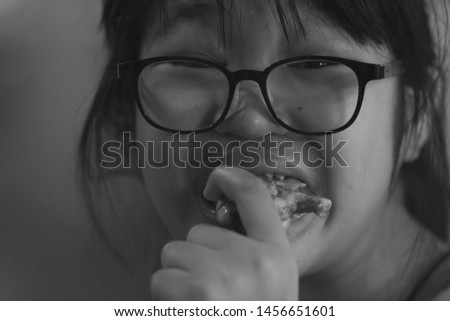 The black and white picture of an Asian girl wearing glasses, eating a grilled chicken, hungry and delicious.