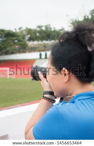 A beautiful woman is using a digital camera on a football field. In the clear air.