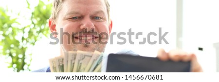 Man making self photo with mobile phone camera posing with pile of US money holding in hands