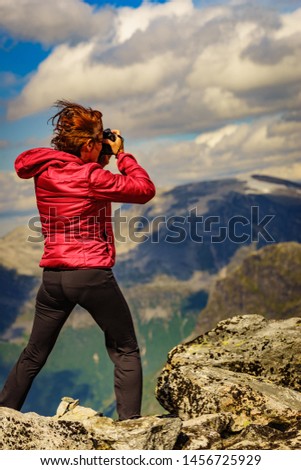 Tourism vacation and travel picture. Female tourist taking photo with camera, enjoying nature from Dalsnibba mountain viewpoint at windy day, Norway.