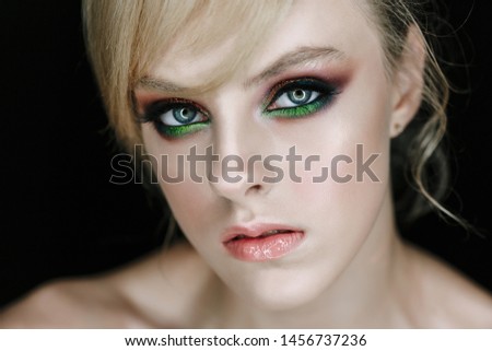 Serious Face Model with Face Make-up Closeup Photo. Stylish Glamour Girl with Angry Gaze and Professional Art Make-up Blonde Hairdo Head-dress Posing on Black Background Studio Portrait